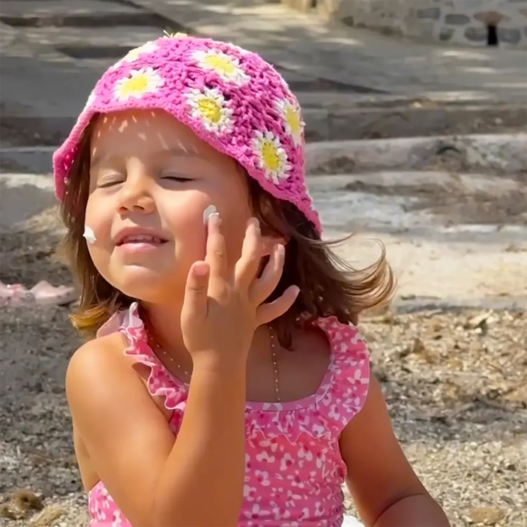 Petite fille appliquant du lait solaire bébé sur son visage, face à la mer.