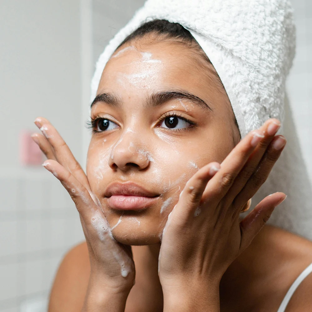 Jeune femme nettoyant son visage avec un gel purifiant anti-imperfections bio devant son miroir