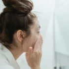 Jeune femme nettoyant son visage avec un gel purifiant anti-imperfections bio devant son miroir