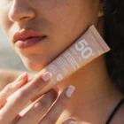 Application crème solaire teintée dorée SPF50+ sur le visage