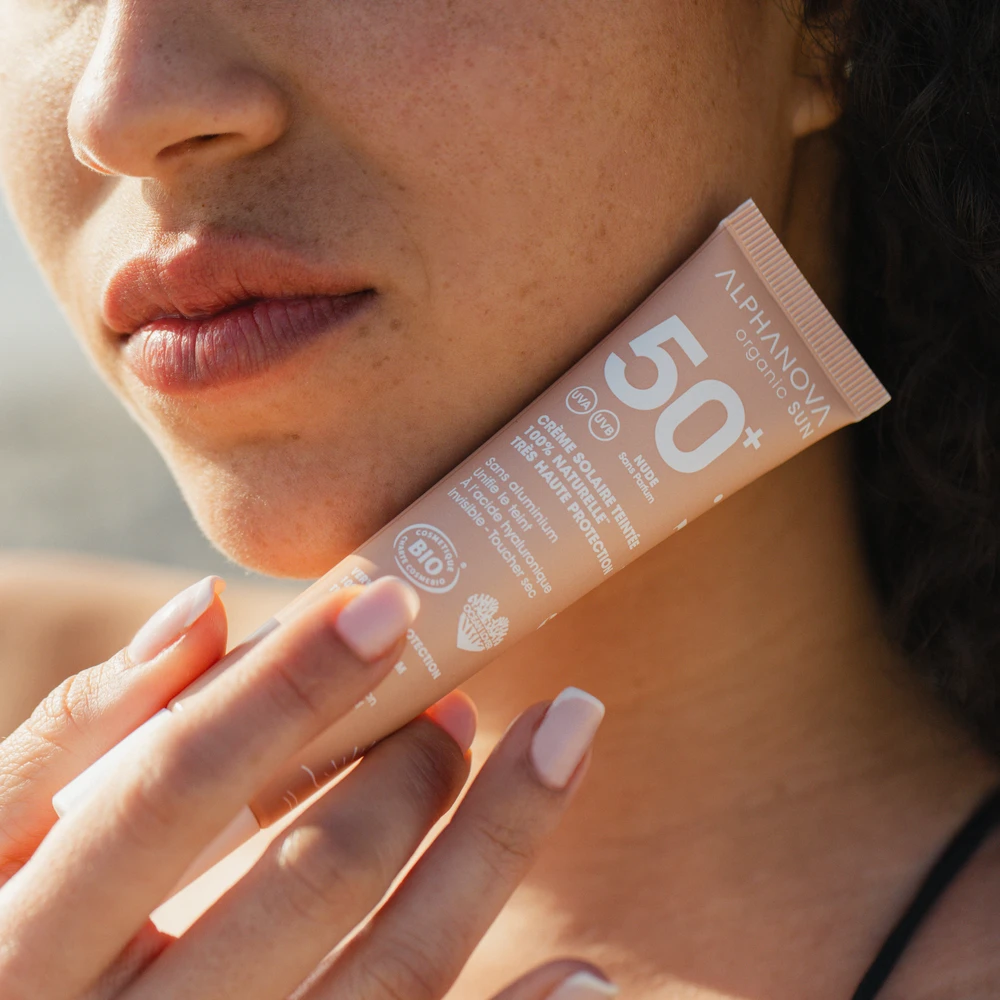 Application crème solaire teintée dorée SPF50+ sur le visage